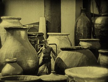 Movie still from “The Thief of Bagdad” (1924), directed by Raoul Walsh – A man standing in front of a group of large pots; Wide shot, High angle