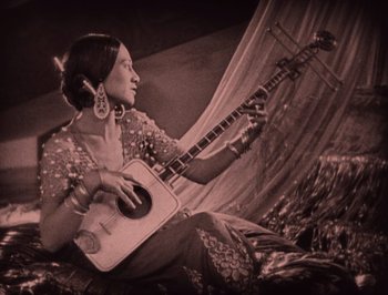 Movie still from “The Thief of Bagdad” (1924), directed by Raoul Walsh – A woman is holding a musical instrument while sitting on the ground; Medium shot, High angle