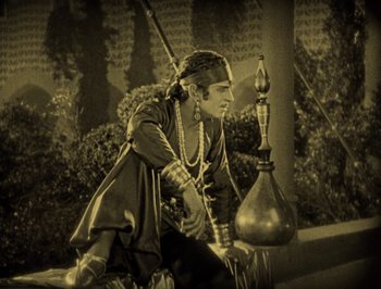 Movie still from “The Thief of Bagdad” (1924), directed by Raoul Walsh – A man sitting next to an urn on top of a wall; Wide shot, High angle
