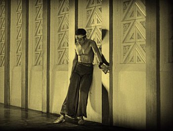 Movie still from “The Thief of Bagdad” (1924), directed by Raoul Walsh – A man standing in front of a wall holding a skateboard; Wide shot, Low angle
