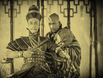 Movie still from “The Thief of Bagdad” (1924), directed by Raoul Walsh – A man and a woman holding a baby in front of an ornate screen; Medium shot, High angle