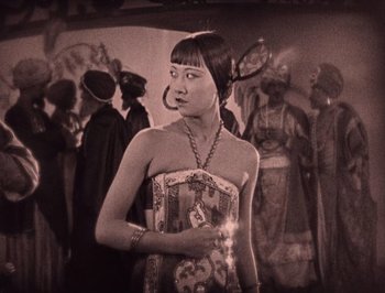 Movie still from “The Thief of Bagdad” (1924), directed by Raoul Walsh – A woman in a dress standing in front of a group of people; Medium shot, High angle