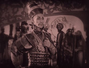 Movie still from “The Thief of Bagdad” (1924), directed by Raoul Walsh – A man dressed in a costume with other people in the background; Medium shot, High angle