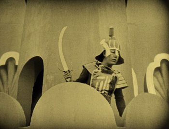 Movie still from “The Thief of Bagdad” (1924), directed by Raoul Walsh – A man in a costume holding two swords; Wide shot, High angle