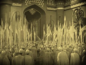 Movie still from “The Thief of Bagdad” (1924), directed by Raoul Walsh – A crowd of people are gathered in front of an archway; Extreme Wide shot, High angle