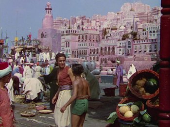 Movie still from “The Thief of Bagdad” (1940), directed by Alexander Korda – A woman and a child are standing in front of a market; Wide shot, High angle