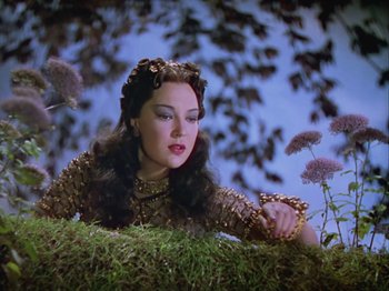 Movie still from “The Thief of Bagdad” (1940), directed by Alexander Korda – A beautiful woman in a gold dress sitting in a field; Medium shot, Low angle