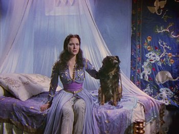 Movie still from “The Thief of Bagdad” (1940), directed by Alexander Korda – A woman and a dog sitting on a bed in a room; Wide shot, High angle