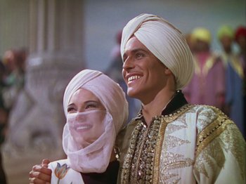 Movie still from “The Thief of Bagdad” (1940), directed by Alexander Korda – A man and a woman wearing turbans smiling for the camera; Medium shot, Low angle
