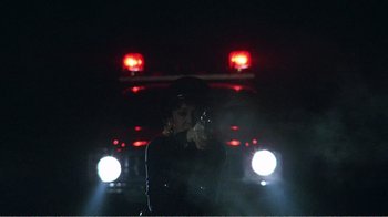 Movie still from “The Thin Blue Line” (1988), directed by Errol Morris – A woman holding a handgun while standing in front of a police car at night; Medium shot, Low angle