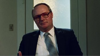 Movie still from “The Thin Blue Line” (1988), directed by Errol Morris – A man in a suit and tie wearing glasses; Close Up shot, Low angle