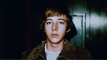 Movie still from “The Thin Blue Line” (1988), directed by Errol Morris – A young man in a brown jacket is looking at the camera; Close Up shot, Overhead angle