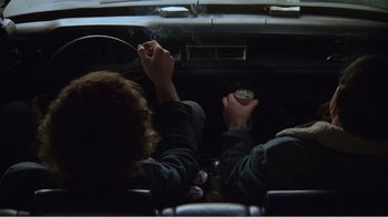 Movie still from “The Thin Blue Line” (1988), directed by Errol Morris – Two people sitting in a car with cigarettes and beer; Medium shot, Overhead angle