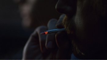 Movie still from “The Thin Blue Line” (1988), directed by Errol Morris – A man with a beard is smoking a cigarette; Extreme Close Up shot, Over the shoulder angle