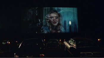 Movie still from “The Thin Blue Line” (1988), directed by Errol Morris – A car driving down a street at night with a movie screen; Wide shot, Over the shoulder angle