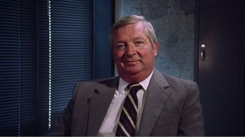 Movie still from “The Thin Blue Line” (1988), directed by Errol Morris – An older man wearing a suit and tie; Close Up shot, High angle