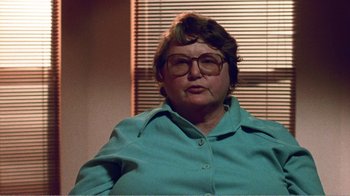Movie still from “The Thin Blue Line” (1988), directed by Errol Morris – An older woman wearing glasses is sitting in a chair; Close Up shot, Over the shoulder angle