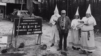 Movie still from “The Thin Blue Line” (1988), directed by Errol Morris – A group of people dressed as kkk standing in front of a sign; Wide shot, High angle