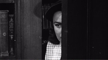Movie still from “The Thin Blue Line” (1988), directed by Errol Morris – A young woman wearing a hat looking through a window; Close Up shot, High angle