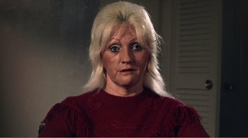 Movie still from “The Thin Blue Line” (1988), directed by Errol Morris – An older woman with blonde hair wearing a red sweater; Close Up shot, High angle