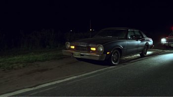 Movie still from “The Thin Blue Line” (1988), directed by Errol Morris – An old car driving down the street at night; Wide shot, Low angle