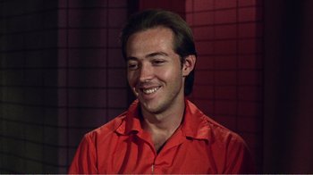 Movie still from “The Thin Blue Line” (1988), directed by Errol Morris – A man in a red shirt smiling for the camera; Close Up shot, High angle