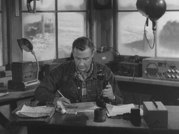 Movie still from “The Thing from Another World” (1951), directed by Howard Hawks – A man sitting at a desk writing on a piece of paper; Medium shot, High angle