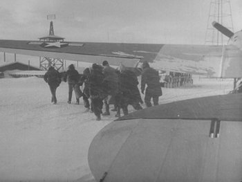 Movie still from “The Thing from Another World” (1951), directed by Howard Hawks – A black and white photo of a group of people walking in the snow near an airplane; Extreme Wide shot, High angle