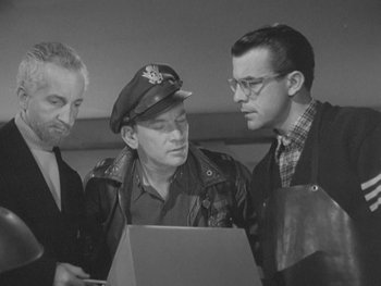 Movie still from “The Thing from Another World” (1951), directed by Howard Hawks – A group of men standing around a laptop computer; Medium shot, High angle