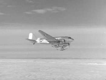 Movie still from “The Thing from Another World” (1951), directed by Howard Hawks – An airplane is flying in the sky on a cloudy day; Extreme Wide shot, High angle