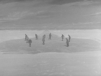 Movie still from “The Thing from Another World” (1951), directed by Howard Hawks – A black and white photo of a group of people standing in the snow; Extreme Wide shot, High angle