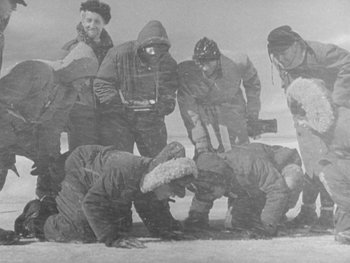 Movie still from “The Thing from Another World” (1951), directed by Howard Hawks – A black and white photo of a group of people on the ground; Wide shot, High angle