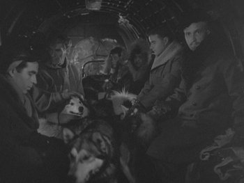 Movie still from “The Thing from Another World” (1951), directed by Howard Hawks – A group of people sitting on top of an airplane; Wide shot, High angle