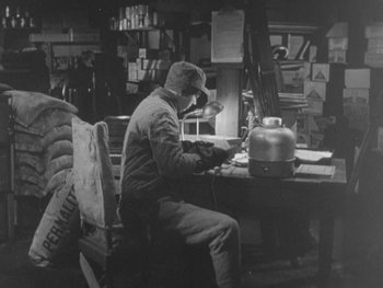 Movie still from “The Thing from Another World” (1951), directed by Howard Hawks – A man sitting at a desk working on a laptop computer; Wide shot, High angle