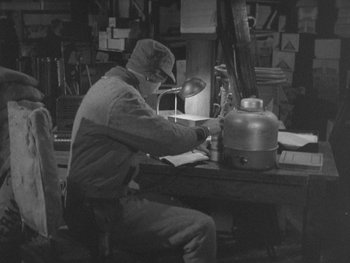 Movie still from “The Thing from Another World” (1951), directed by Howard Hawks – A man sitting at a table in a room; Medium shot, High angle