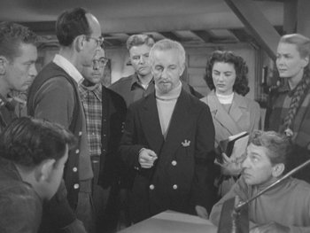 Movie still from “The Thing from Another World” (1951), directed by Howard Hawks – A group of people standing around each other in a room; Medium shot, High angle