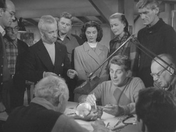 Movie still from “The Thing from Another World” (1951), directed by Howard Hawks – A black and white photo of people gathered around a table; Medium shot, High angle
