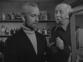 Movie still from “The Thing from Another World” (1951), directed by Howard Hawks – A man in a suit standing next to another man in a tie; Medium shot, Low angle