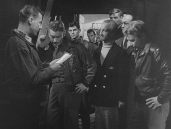 Movie still from “The Thing from Another World” (1951), directed by Howard Hawks – A group of men standing around each other in front of a building; Medium shot, Over the shoulder angle