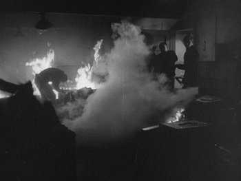 Movie still from “The Thing from Another World” (1951), directed by Howard Hawks – A black and white photo of people in a room with a fire; Wide shot, High angle