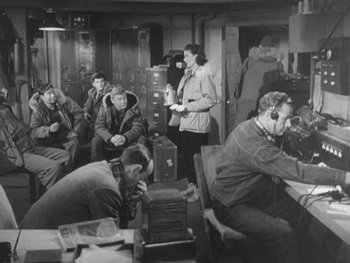 Movie still from “The Thing from Another World” (1951), directed by Howard Hawks – A group of people sitting in a room with boxes; Medium shot, High angle