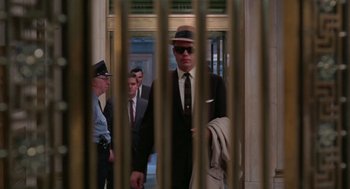 Movie still from “The Thomas Crown Affair” (1968), directed by Norman Jewison – A group of men in suits and hats standing in front of a metal gate; Wide shot, Low angle