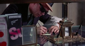 Movie still from “The Thomas Crown Affair” (1968), directed by Norman Jewison – A man in a hat and sunglasses working on something; Close Up shot, Low angle