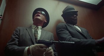 Movie still from “The Thomas Crown Affair” (1968), directed by Norman Jewison – A man in a suit and a man in a hat holding a gun; Medium shot, Low angle