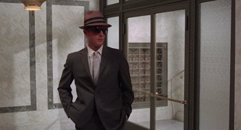 Movie still from “The Thomas Crown Affair” (1968), directed by Norman Jewison – A man in a suit and hat standing in front of a door; Medium shot, Low angle