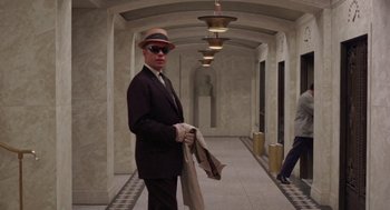 Movie still from “The Thomas Crown Affair” (1968), directed by Norman Jewison – A man in a suit and hat holding a jacket; Wide shot, Low angle