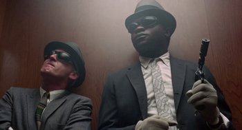 Movie still from “The Thomas Crown Affair” (1968), directed by Norman Jewison – A man in a suit and tie next to another man in a suit and tie; Medium shot, Low angle