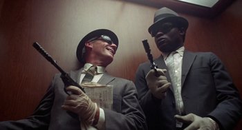 Movie still from “The Thomas Crown Affair” (1968), directed by Norman Jewison – A man in a suit and a man in a hat holding guns; Medium shot, Low angle