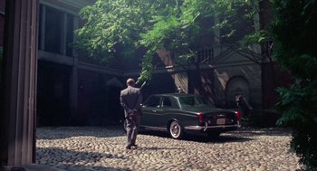 Movie still from “The Thomas Crown Affair” (1968), directed by Norman Jewison – A man standing next to a car in a driveway; Wide shot, High angle