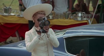 Movie still from “The Thomas Crown Affair” (1968), directed by Norman Jewison – A woman wearing a white suit and a white hat taking a picture; Medium shot, Low angle